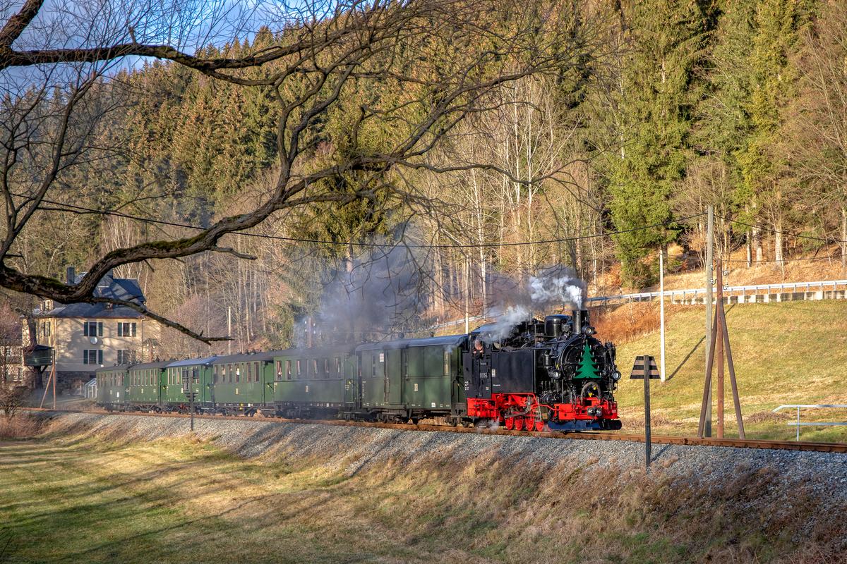 Zum zweiten Advent 2018 gab es nicht nur Zweizugbetrieb und übervolle Züge zur Mettenschicht am Andreas-Gegentrum-Stolln, sondern sogar Sonne. In dieser wartete hier die Lok 99 1715-4 mit ihrem Zug an der Trapeztafel des Bahnhofs Schmalzgrube auf Einfahrt.