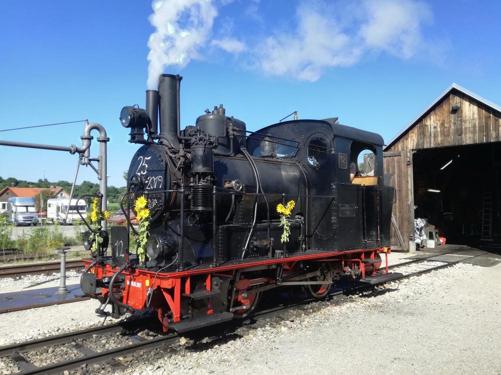 Am Morgen des 11. August 2019 wartet die geschmückte Lok 12 der Härtsfeld-Museumsbahn vor der Neresheimer Lokremise auf ihren ersten Einsatz an diesem Tag. Eine Kreideanschrift an der Rauchkammer würdigt ihren 25-jährigen Dienst als Museumslokomotive.