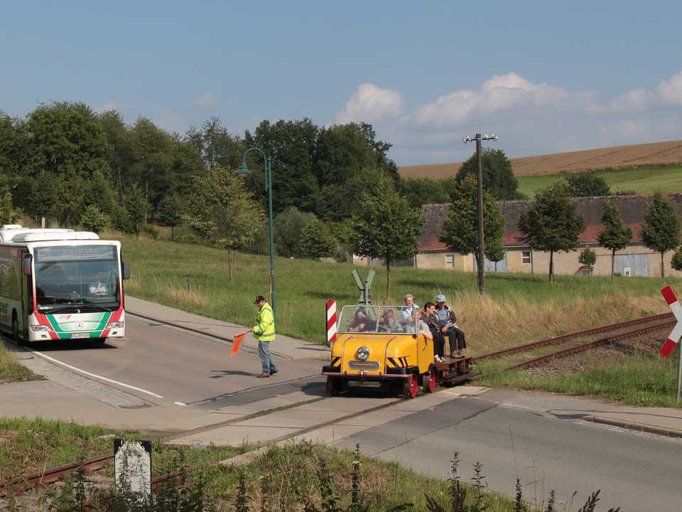 Am Bahnübergang Penig legt die Busbahn eine Pause ein, um den Schienentrabi passieren zu lassen. Wie so oft haben auf dem Eisenbahnfahrzeug mehr Gäste Platz genommen als in der „Gummikonkurrenz“.
