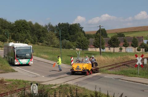 Am Bahnübergang Penig legt die Busbahn eine Pause ein, um den Schienentrabi passieren zu lassen. Wie so oft haben auf dem Eisenbahnfahrzeug mehr Gäste Platz genommen als in der „Gummikonkurrenz“.