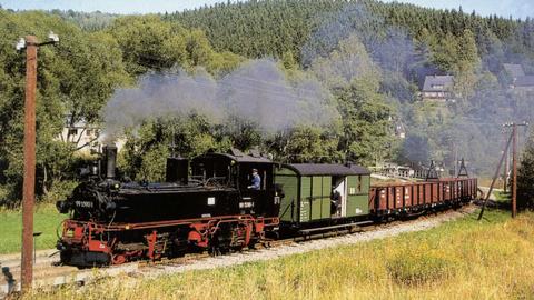 Am 4. September 2004 hatten bei der Preßnitztalbahn wieder einmal die Güterzüge Vorrang. Fotografin Veronika Michael lichtete diese Zuggarnitur mit 99 590, dem zweiachsigen Packwagen 97-30-06 sowie mehreren 00 an bekannter Fotostelle hinter Schmalzgrube ab.