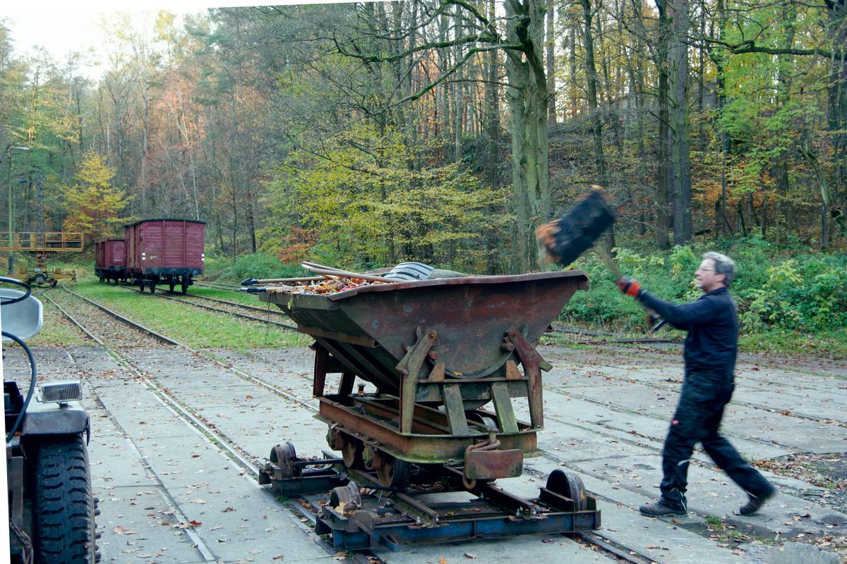 Beladen eines Muldenkippers mit Brennholz. Der 600-mm-Wagen steht dabei auf einem regelspurigen Eigenbau-„Rollwagen“. Auf diesem können die Feldbahnwagen im Regelspurgleisfeld des Feldbahnmuseums Herrenleite verschoben werden.