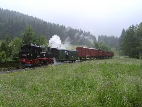 Einfahrt des mit drei beladenen Rollfahrzeugen bestückten Güterzuges in den Bahnhof Schmalzgrube bei strömendem Regen.
