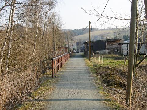 Das Bild rechts vom April 2003 zeigt den Blick entlang des Bahndamms vom km 13,38 in Richtung der Station Oberschmiedeberg. Das Stationsgebäude ist links hinter den Bäumen zu erkennen. Der graue Wagenkasten rechts stand dort schon zu Betriebszeiten, die anderen Schuppen sind inzwischen beseitigt.